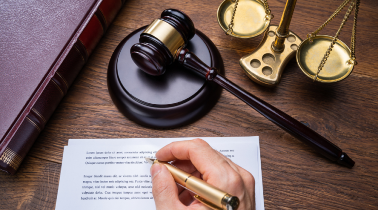 L'immagine rappresenta un tavolo di un general counsel: sopra ci sono un foglio, un martello da giudice e una bilancia.